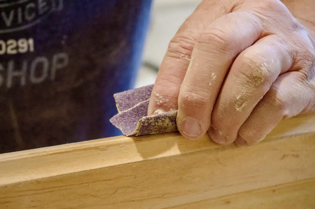 a-closeup-view-of-an-adult-male-hand-holding-sandpaper-that-is-sanding-a-wooden-cabinet-door