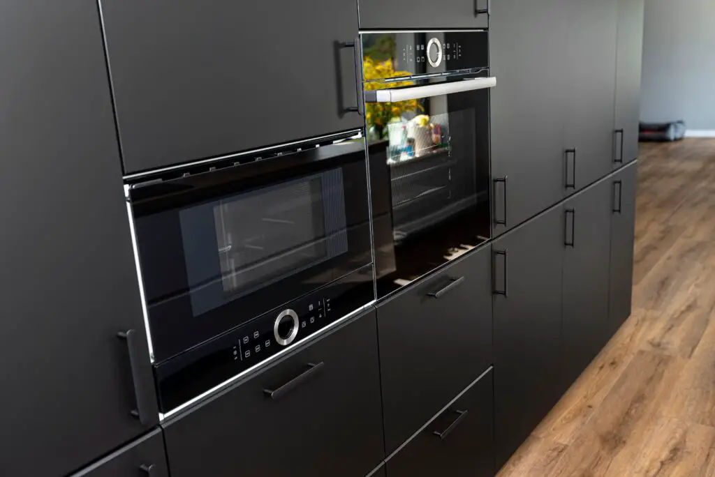Modern kitchen with black fronts, built in oven and microwave, vinyl panels on the floor.